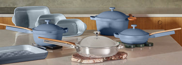 A set of blue ceramic cookware and clear glass pan with wooden handles displayed on a kitchen countertop.
