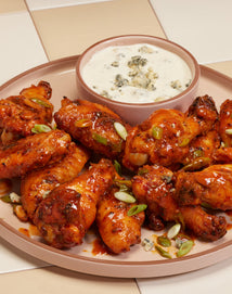A plate of saucy chicken wings garnished with green onions, served with a bowl of blue cheese dipping sauce.