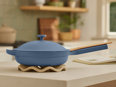 Blue lidded pan with a wooden handle resting on a wavy, light-colored trivet on a kitchen counter.