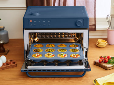 A navy blue countertop oven with its door open, containing a tray of twelve individual egg-based breakfast muffins.