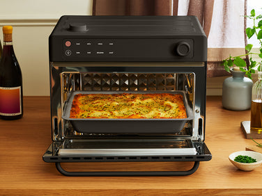 A black countertop oven with the door open, containing a rectangular baking dish filled with a baked potato casserole.