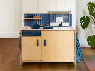 A wooden toy kitchen featuring a blue-tiled backsplash, a sink with a water dispenser, and a stovetop with a blue toy pot.