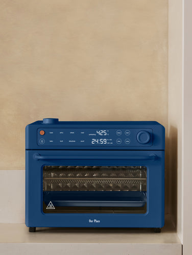 A blue countertop air fryer oven sitting on a kitchen counter next to bottles of condiments and a potted plant.