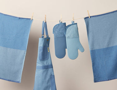 Blue Home Cook Apron, Hot Mitts, and Double Dish Towels hanging from a clothesline