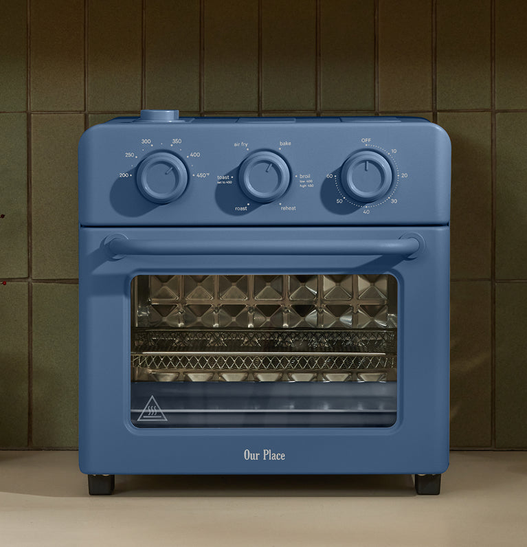 Blue toaster oven on a kitchen counter with decorative items in the background