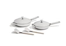 Two stainless steel frying pans with lids and two white spatulas with light-colored handles are placed on a white background.