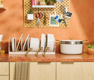 Kitchen counter with pots, pans, and a pegboard with tools and decor on an orange wall.