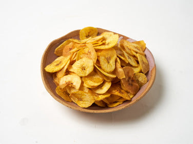 A ceramic bowl filled with yellow, crispy plantain chips on a plain white background.