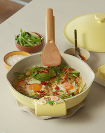 Yellow ceramic dish with food, wooden spoon, and small bowls on a light surface