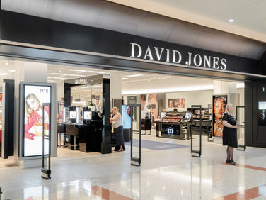 Entrance to a David Jones department store, featuring a large black wall with gold lettering and visible store interior in the background.