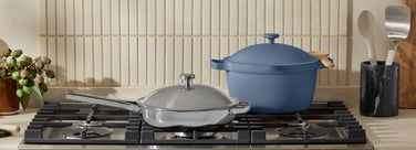 Blue cast iron pot and silver pans on a stove with kitchen utensils in the background.