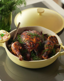 Roasted chicken in a yellow ceramic dish on a reflective surface
