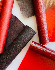 Several rolls and flat sheets of red fruit leather arranged on a white surface.