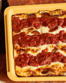 Rectangular Detroit-style pizza with pepperoni, melted cheese, and two strips of red sauce in a yellow baking pan.