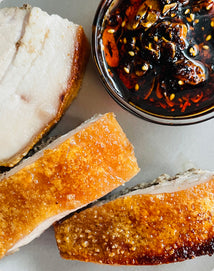 Slices of crispy pork belly served with a side of chili oil.