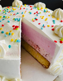 Layered ice cream cake with a slice removed, topped with white frosting swirls and multicolored sprinkles.