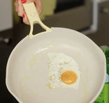 Fried egg in a white frying pan held by a hand with red nail polish.