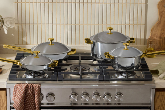Four chrome/gold pots and pans on a stovetop