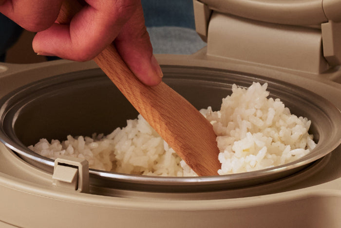 A wooden spatula scooping rice in a rice cooker