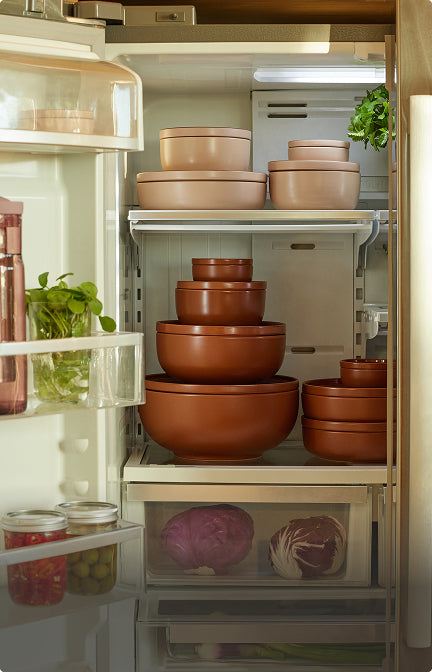 A set of nested ceramic bowls in terracotta and light beige colors, neatly organized inside an open refrigerator.