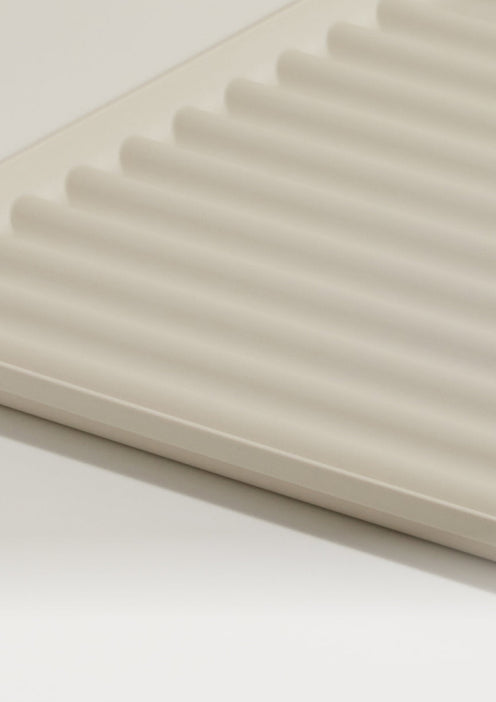 A close-up of a beige, ridged plastic or ceramic tray with evenly spaced grooves, set against a plain background.
