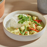 A bowl of white rice served with tofu, green beans, red pepper slices, and green curry, garnished with cilantro.