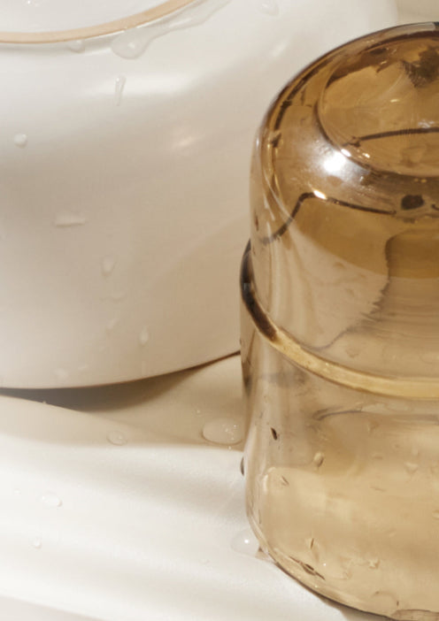A close-up of a translucent brown container and a white container with water droplets on their surfaces, placed on a light-colored background.