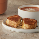 A grilled cheese sandwich cut in half with melted cheese, served on a plate next to a bowl of tomato soup topped with grated cheese.
