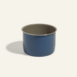 A blue, cylindrical metal pot with measurement markings on the inside, placed on a light-colored surface.