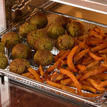 A metal air fryer basket containing several round falafel and a portion of sweet potato fries.