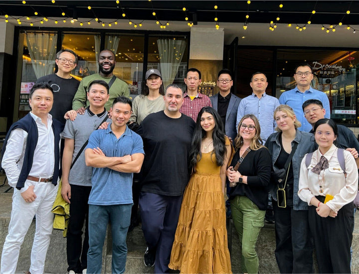 A group of sixteen people pose together outside a restaurant under string lights, smiling at the camera.