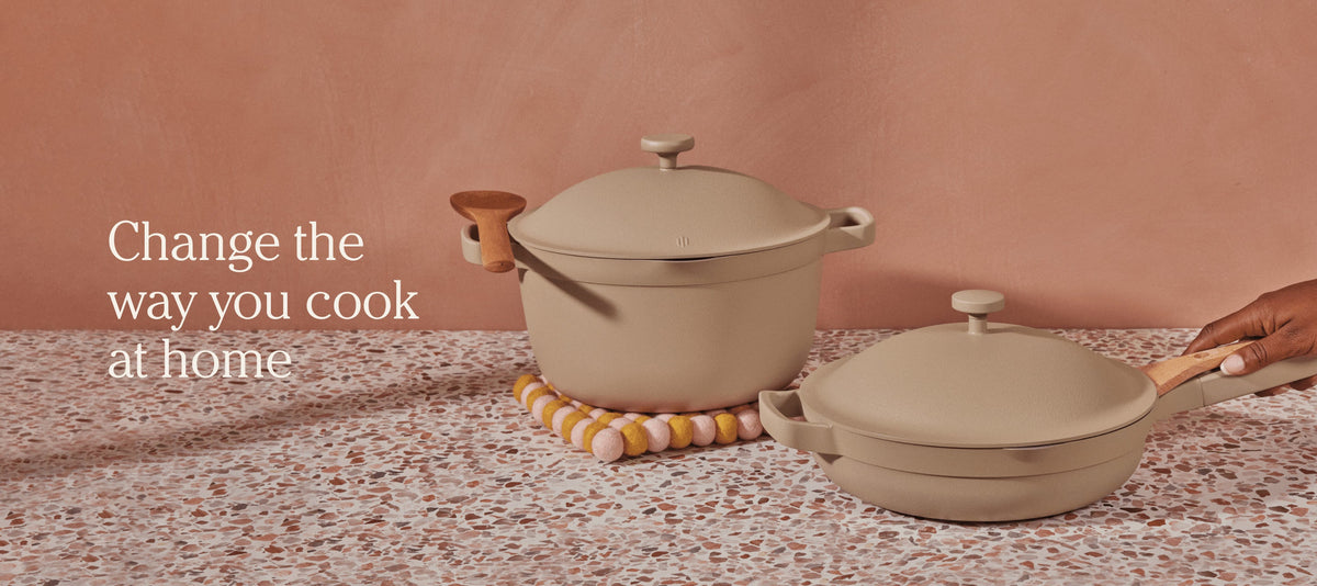 Translation missing: en.Two beige cookware pieces, a lidded pot and a pan with wooden handles, on a terrazzo countertop next to the text Change the way you cook at home