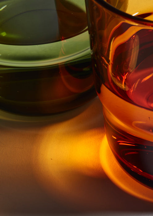 Close-up of two glass cups, one green and one amber, casting colored reflections and shadows on a light surface.