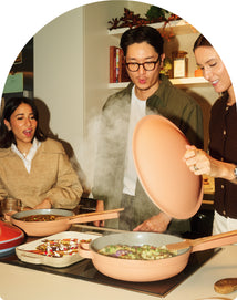 People cooking together in a kitchen with a pink pan