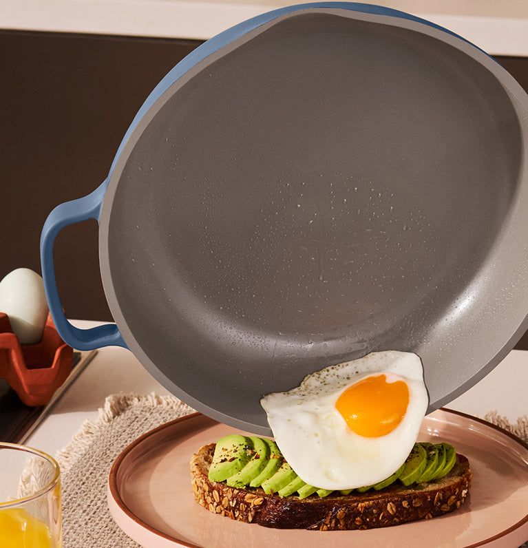 Gray frying pan with blue handle on a kitchen counter with toast and avocado spread.