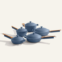 The Cookware Set+ features five blue nonstick pots and pans with matching lids and wooden handles, arranged on a light background to highlight this stylish ceramic cookware, ideal for modern kitchens.
