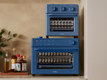 Two blue Our Place countertop ovens stacked on a kitchen counter next to bottles of condiments.