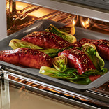 Glazed salmon fillets with bok choy on a baking sheet inside an oven.