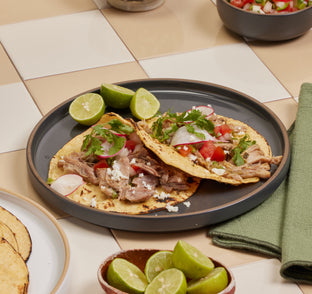 Tacos on a plate with lime wedges on a checkered tablecloth