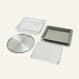 The Wonder Oven Pro Chef’s Kit features four versatile inserts: a rectangular pan, perforated tray, wire rack, and mesh basket on a light background.