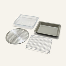 The Wonder Oven Pro Chef’s Kit features four versatile inserts: a rectangular pan, perforated tray, wire rack, and mesh basket on a light background.