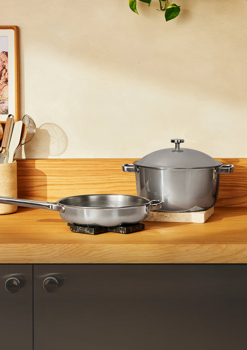 A stainless steel frying pan and a lidded stockpot on a wooden kitchen counter.
