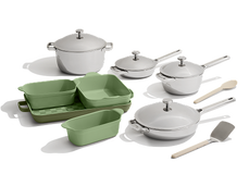 A set of white cookware with silver handles, green baking dishes, a green loaf pan, a beige spatula, and a beige wooden spoon arranged on a light surface.