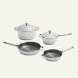 Two pots with lids and two skillets with metallic interiors and light-colored exteriors, displayed as a Titanium Pro Cookware Set 2.0.