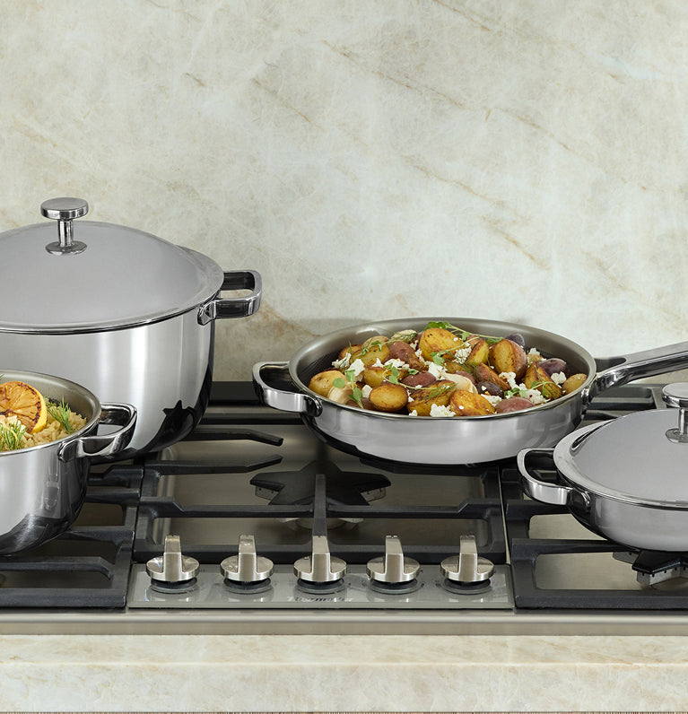 Set of stainless steel cookware on a gas stove with food inside