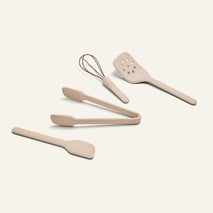 The Mini Utensil Essentials set features five beige silicone tools—a whisk, spatula, slotted turner, tongs, and another spatula—on a light background.