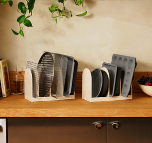 Two countertop organizers holding baking sheets, cooling racks, and muffin tins.