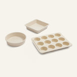 The Wonder Oven Pro Baker’s Kit—featuring a square pan, round pan, and 12-cup muffin tin in cream ceramic—rests on a neutral background.