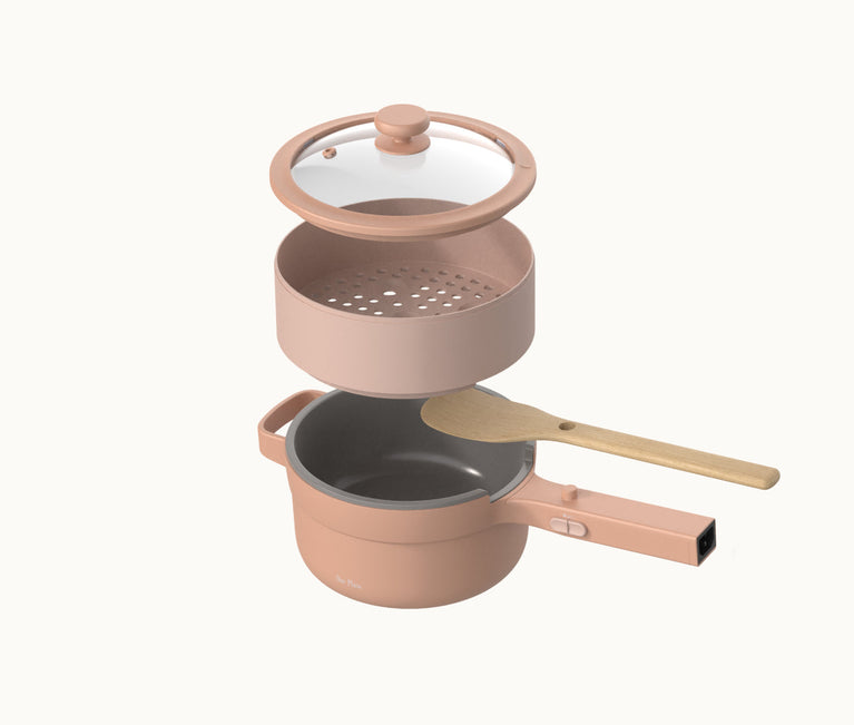 A pink saucepan with a matching lid, a steamer insert, and a wooden spoon resting on top, all set against a plain white background.