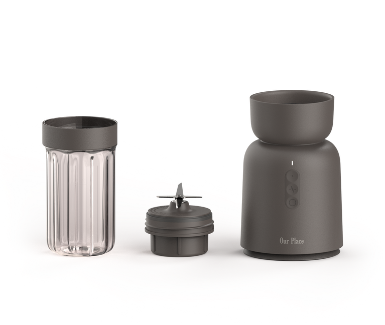 A compact blender set with a clear blending cup, a blade attachment, and a dark gray motor base labeled “Our Place” on a white background.